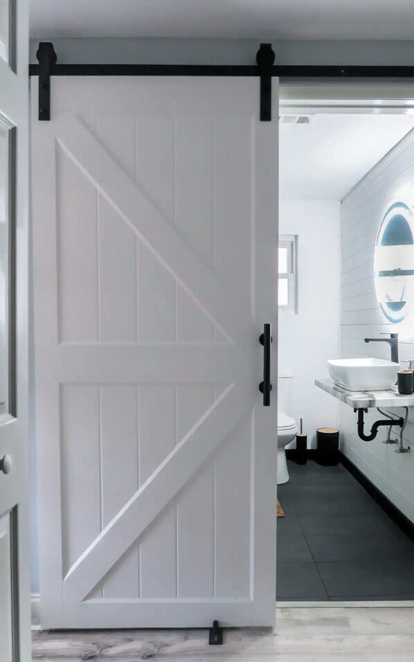 Un baño moderno con una puerta blanca, un espejo grande y un lavabo blanco.