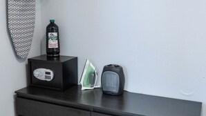 Een opgeruimde opslagruimte met een kledingrek, een fles Tiki Bitefighter, een strijkijzer en een speaker.