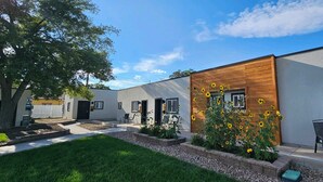 Un bâtiment moderne à la façade en bois, un petit jardin avec des tournesols et un ciel d’un bleu limpide.