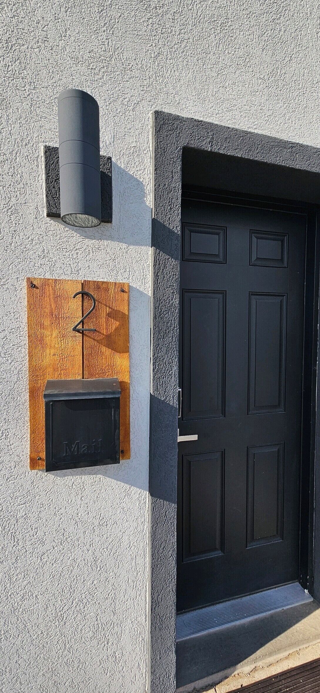 A black door with a mailbox and a number 2 sign on a textured wall.