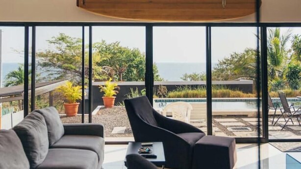 A modern living room with a large window overlooking a pool and greenery.