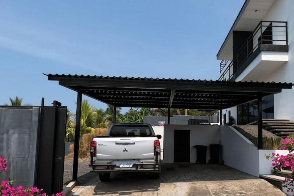 Una camioneta pickup blanca estacionada bajo un techo, con un edificio moderno al fondo.