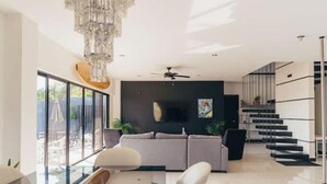 A modern living room with a grey sofa, a chandelier, and a staircase.