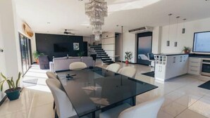 A modern kitchen with a glass dining table, white chairs, and a chandelier.