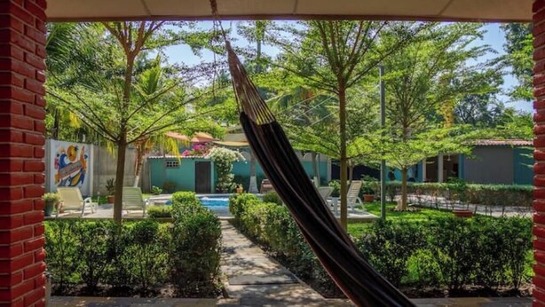 Uma rede num pátio com piscina, rodeada por vegetação e um edifício com um mural.