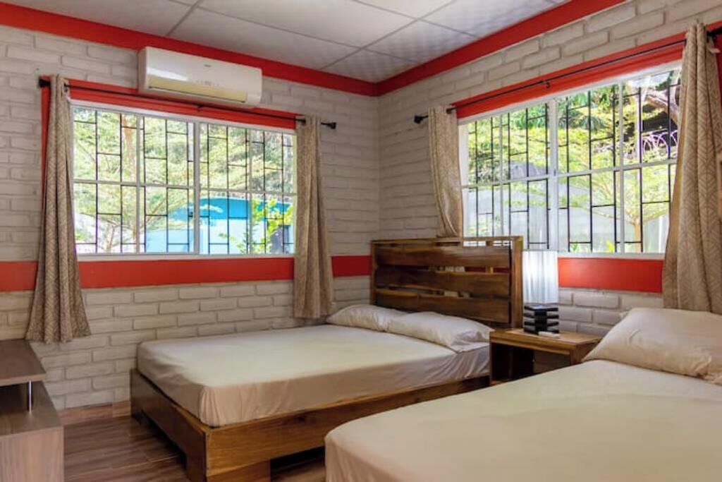 A room with two beds, a wooden headboard, a small table, and a window with curtains.