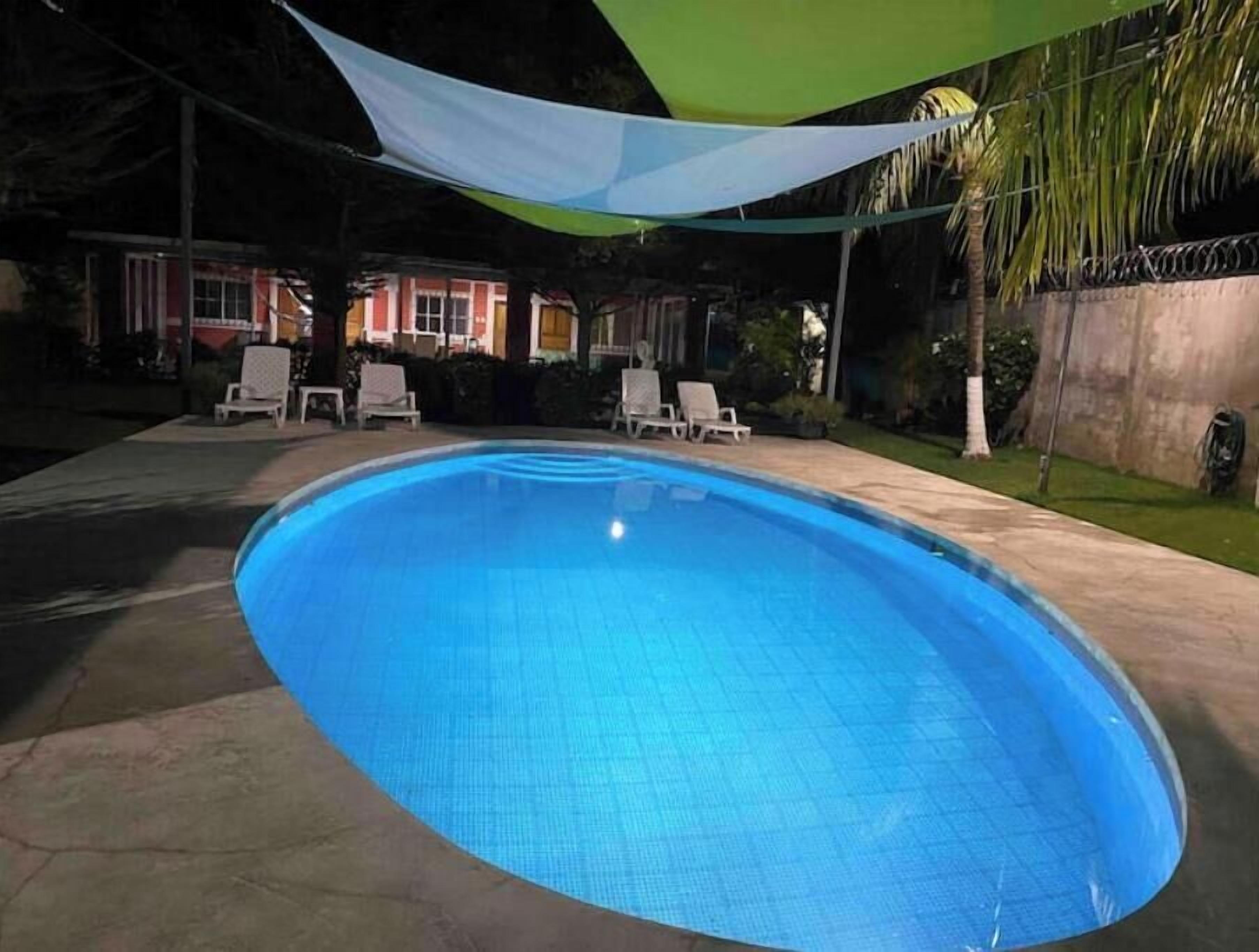 Piscina com borda em azulejo, rodeada por espreguiçadeiras e uma área coberta com toldo verde e branco.