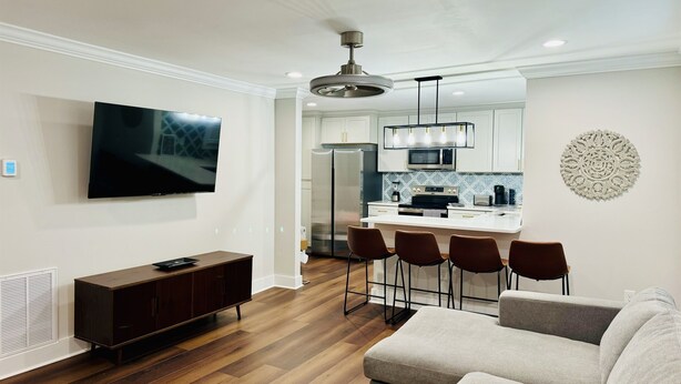 A modern living room with a TV, dark wood flooring, a brown entertainment unit, and a grey sofa.