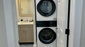 A laundry room with a stacked washer and dryer, a sink with a mirror, and a light fixture above the mirror.