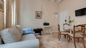 Una sala de estar con un sofá, una mesa de comedor con sillas, un televisor montado en la pared y un cuadro enmarcado.