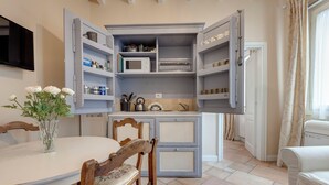 Una cocina compacta con armarios abiertos, una mesa de comedor con sillas y un jarrón con flores.