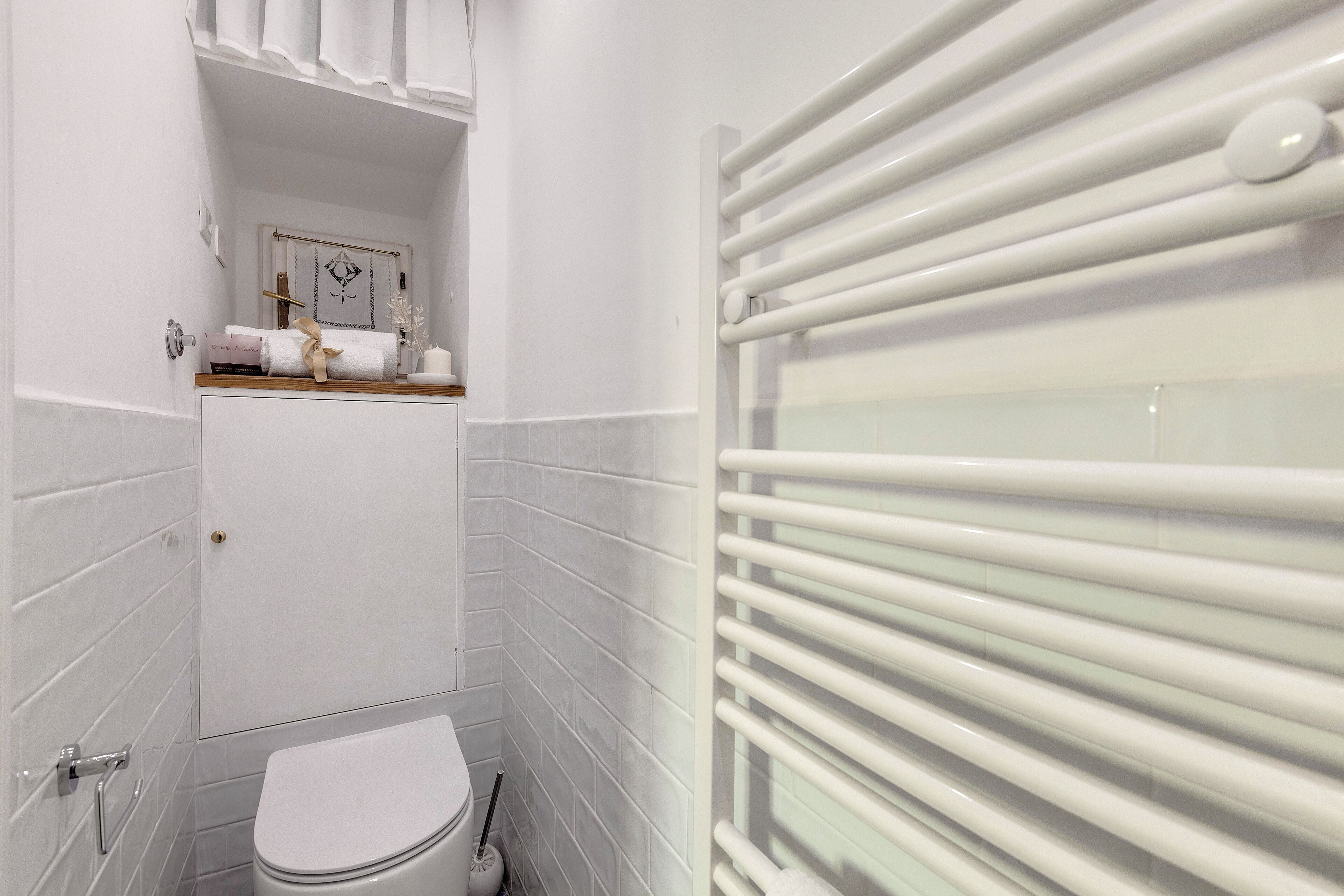 A modern bathroom with white tiles, a toilet, a towel rack, and a mirror.