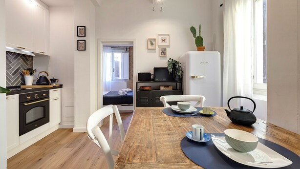 A modern kitchen with white cabinets, a wooden dining table, and a refrigerator. - Mamo Florence - Aida Apartment (Florence)