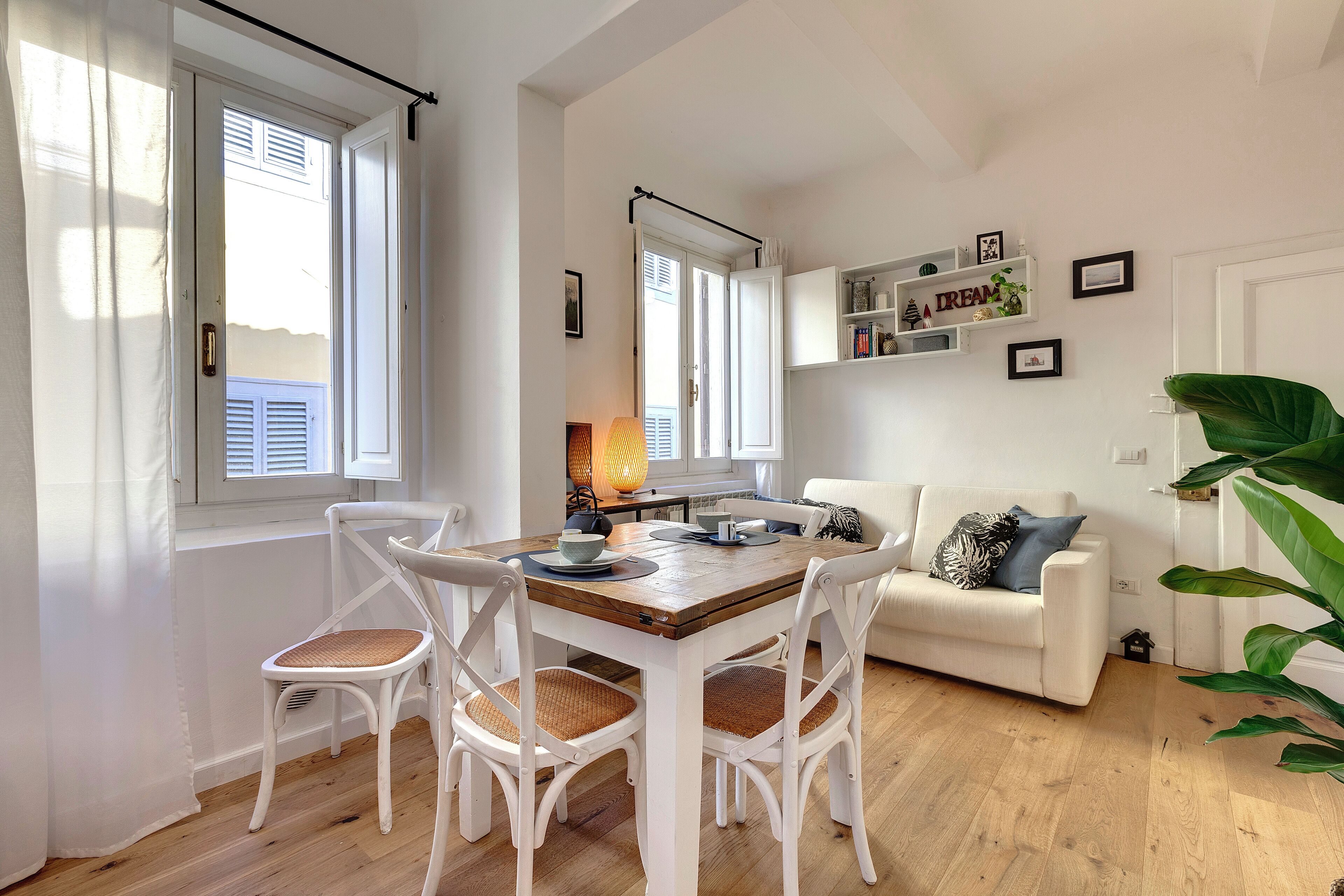 A modern living room with a dining table, white chairs, a sofa, and a large plant.