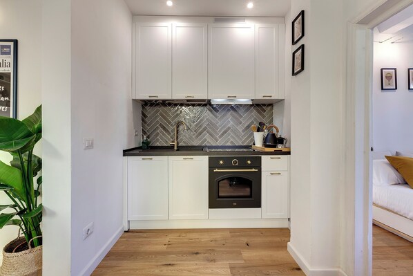 A compact kitchen with white cabinets, a black oven, and a herringbone-patterned backsplash.