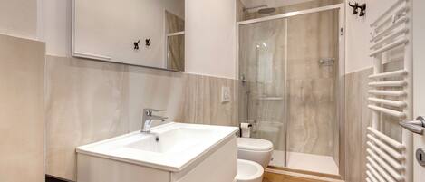 A modern bathroom with a white sink, toilet, and glass shower enclosure.