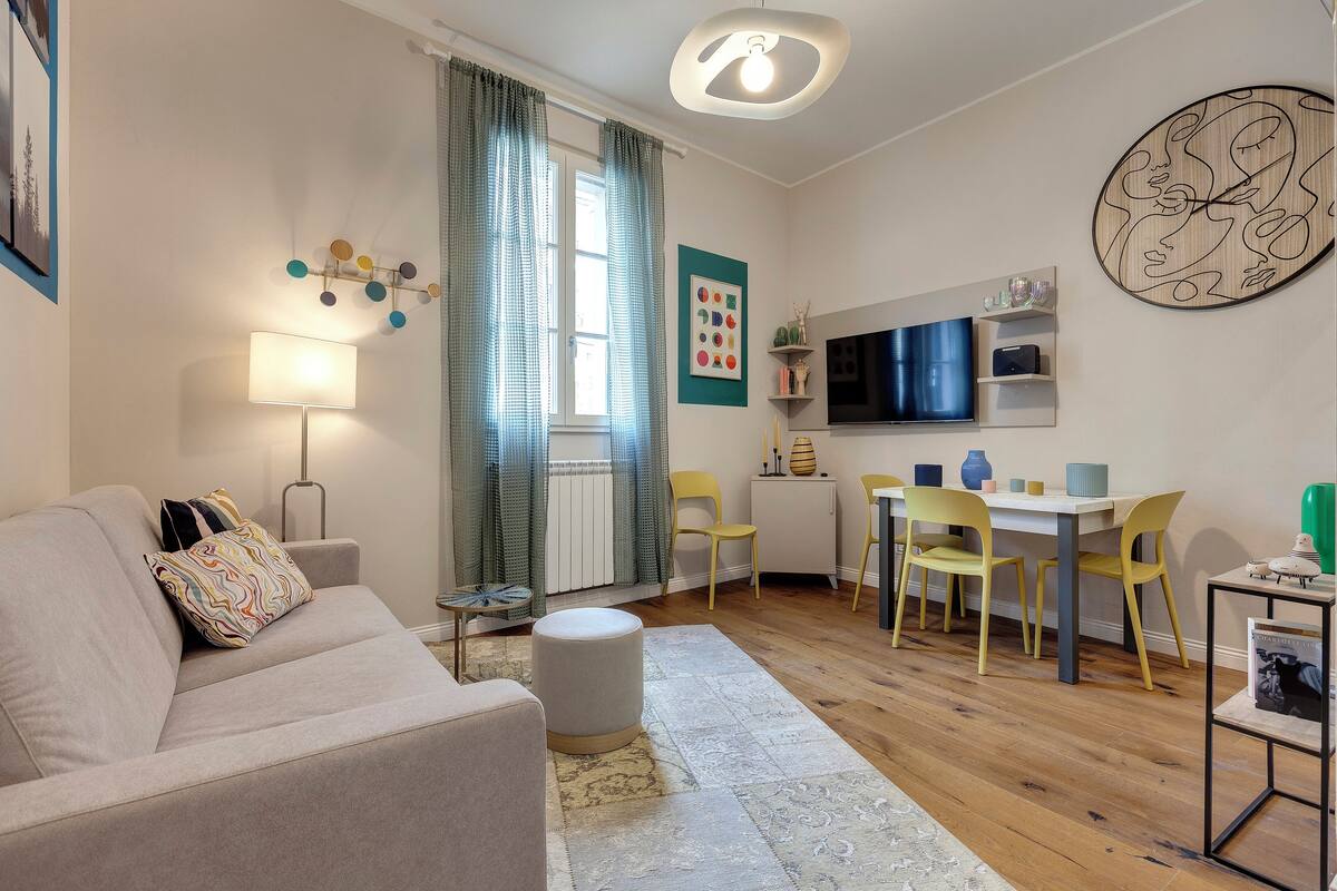 Ein modernes Wohnzimmer mit einer Couch, einem Hocker und einem Essbereich mit Stühlen und einem Tisch.