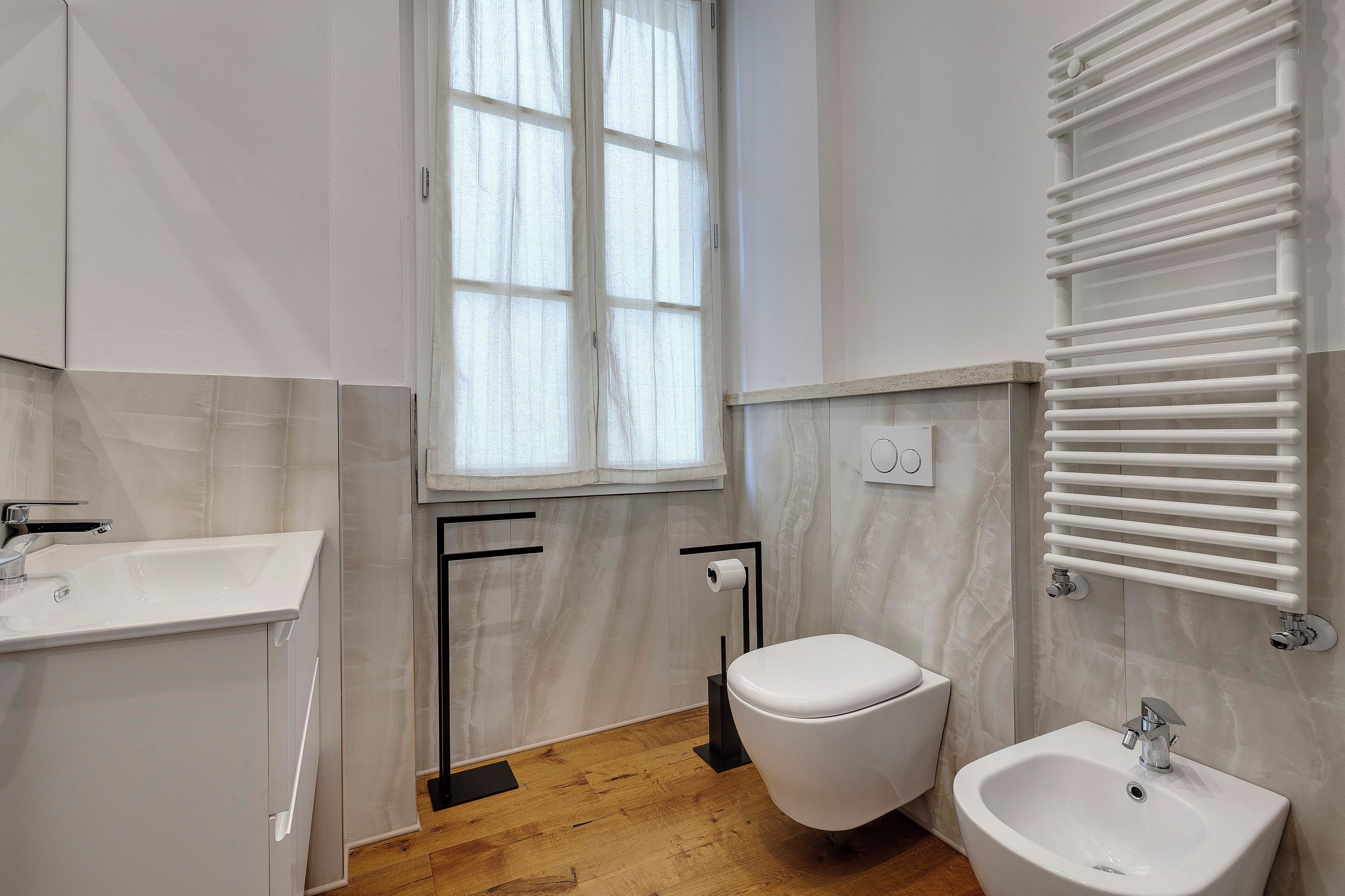A modern bathroom with a toilet, bidet, sink, and towel rack.