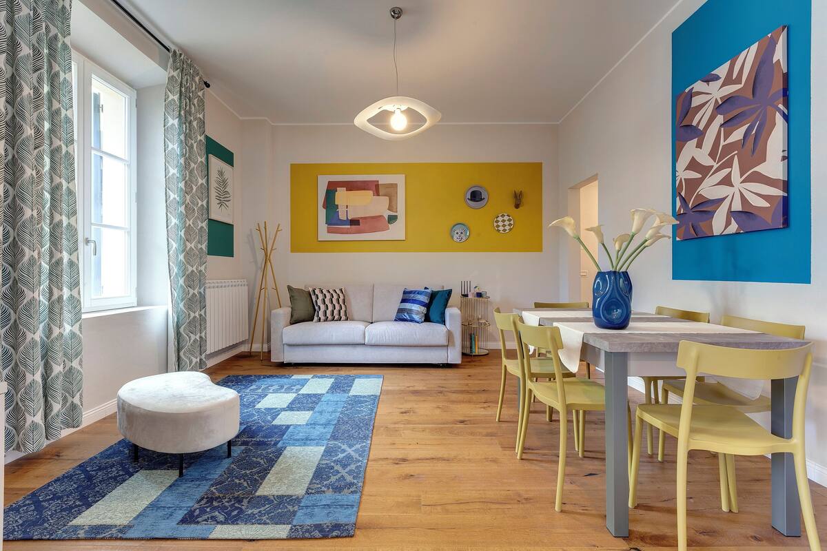 Ein Wohnzimmer mit einer Couch, einem Hocker und einem Essbereich mit Stühlen und einem Tisch.