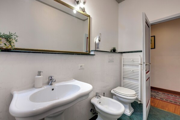 A bathroom with a large mirror, a sink, a bidet, and a toilet.