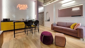 Een moderne keuken met een neonbord, een eethoek met zwarte stoelen, een houten vloer en een woonkamer met een bank en poefs.