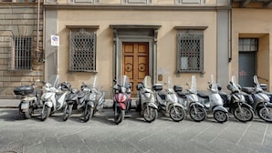Een rij geparkeerde scooters voor een gebouw met een houten deur en tralies.