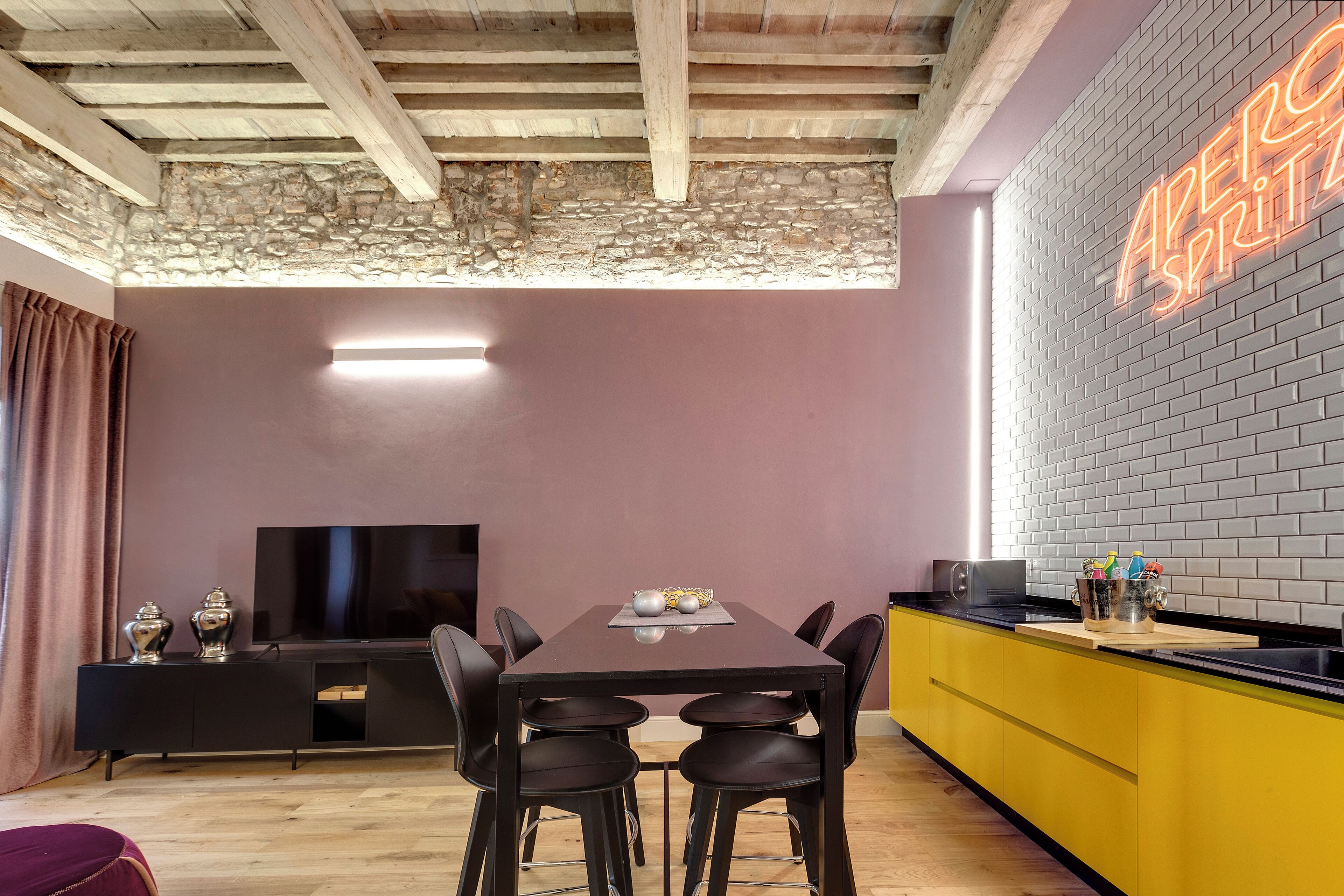 A modern kitchen with a black countertop, yellow cabinets, and a neon sign on the wall.