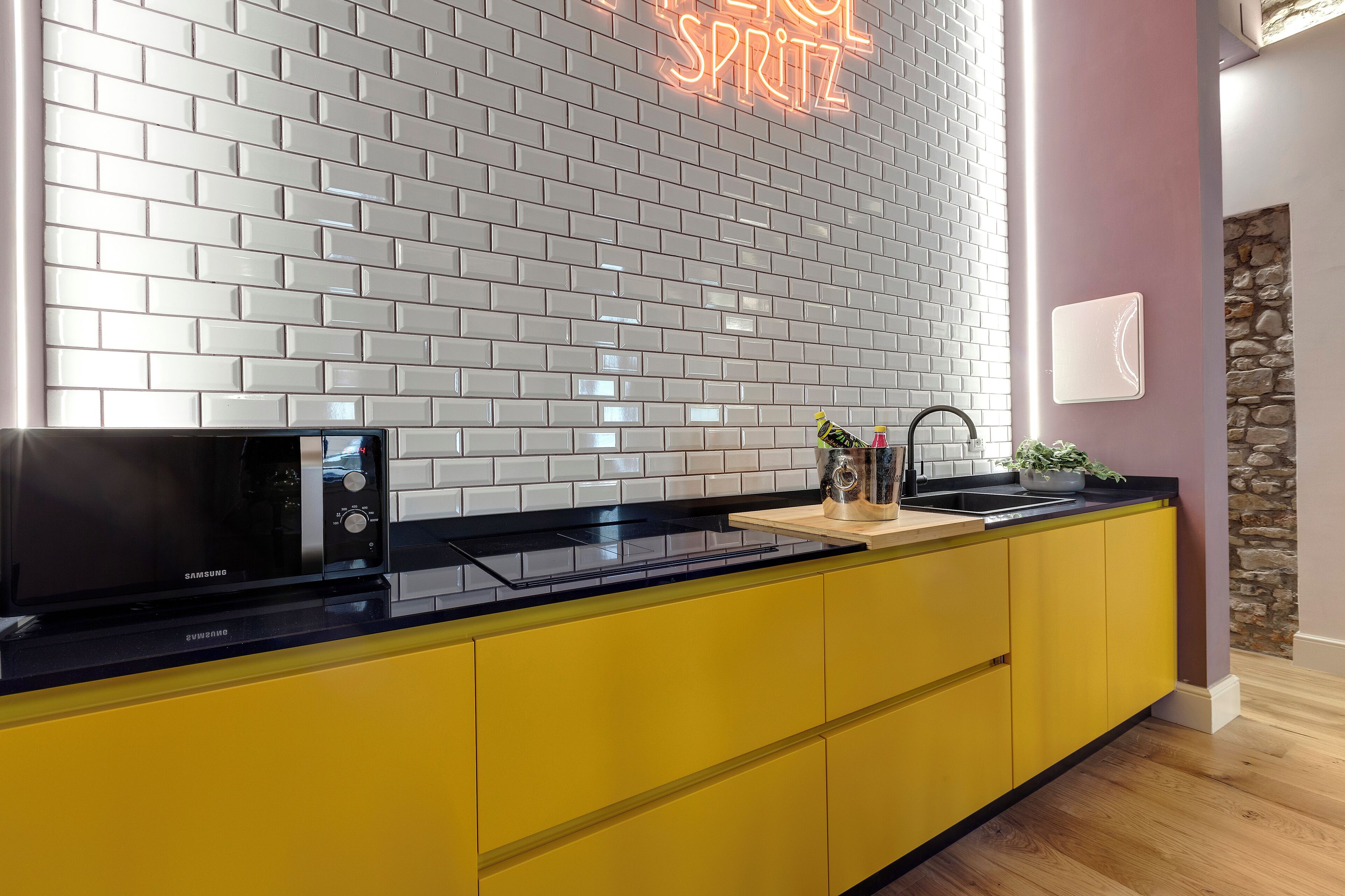 A modern kitchen with a black microwave, yellow cabinets, and a neon sign on the wall.
