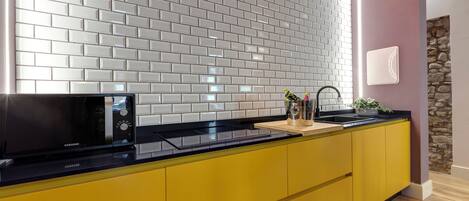 A modern kitchen with a black microwave, yellow cabinets, and a neon sign on the wall.