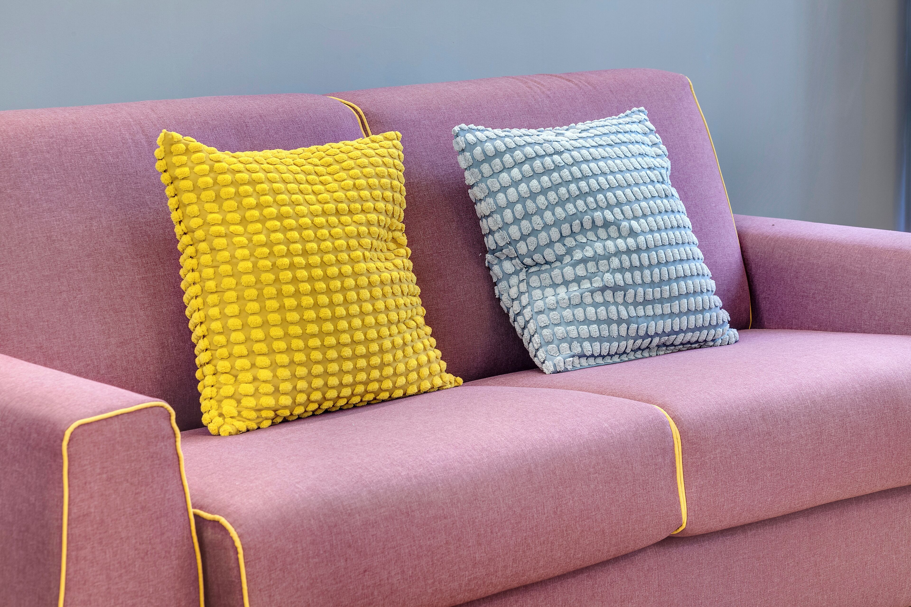 A purple sofa with two textured pillows, one yellow and one blue.