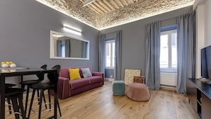 Een moderne woonkamer met een stenen plafond, een rode bank met kussens, een roze poef en een grijze bank.