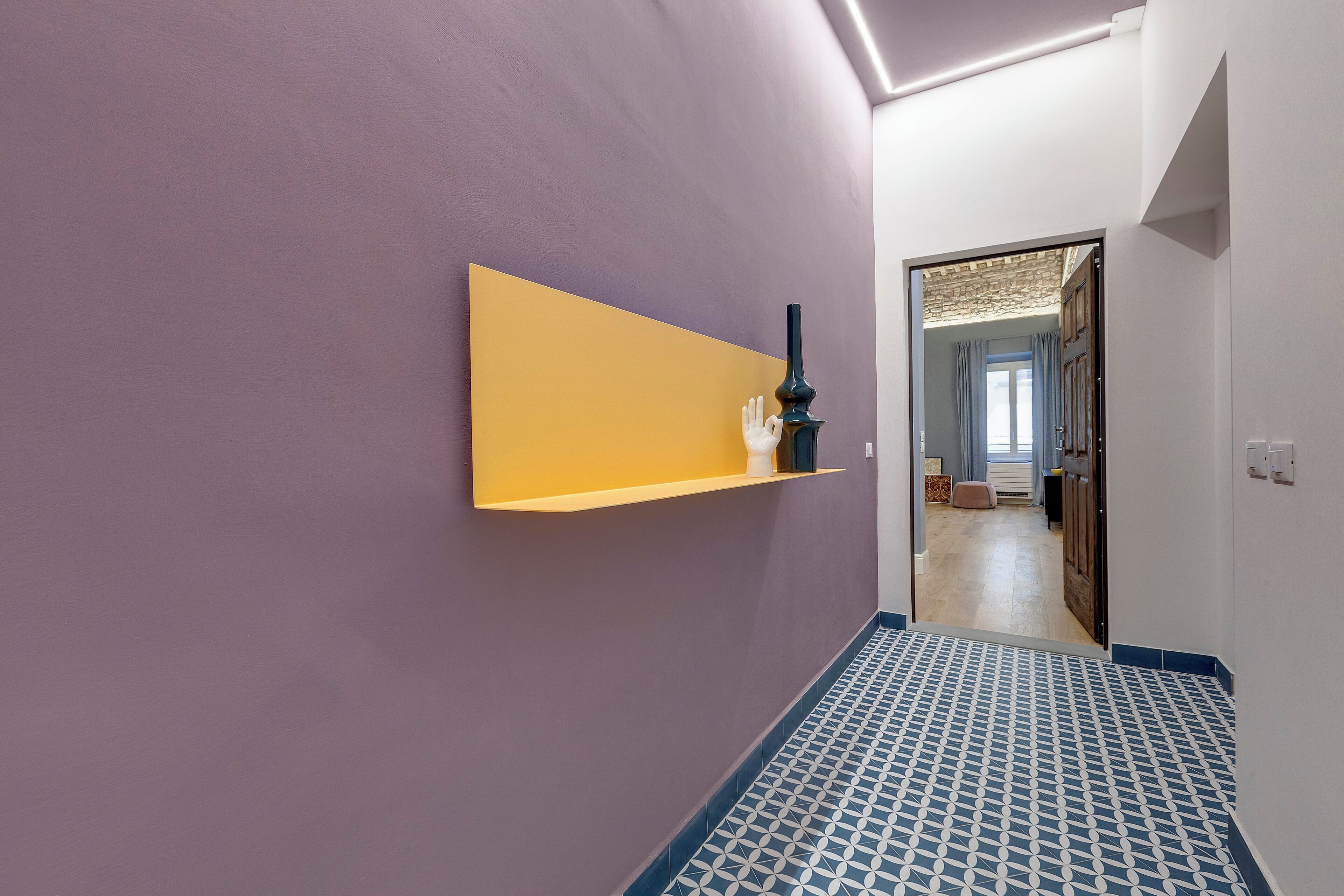 Un couloir avec un mur violet, une étagère jaune et un sol à motifs.
