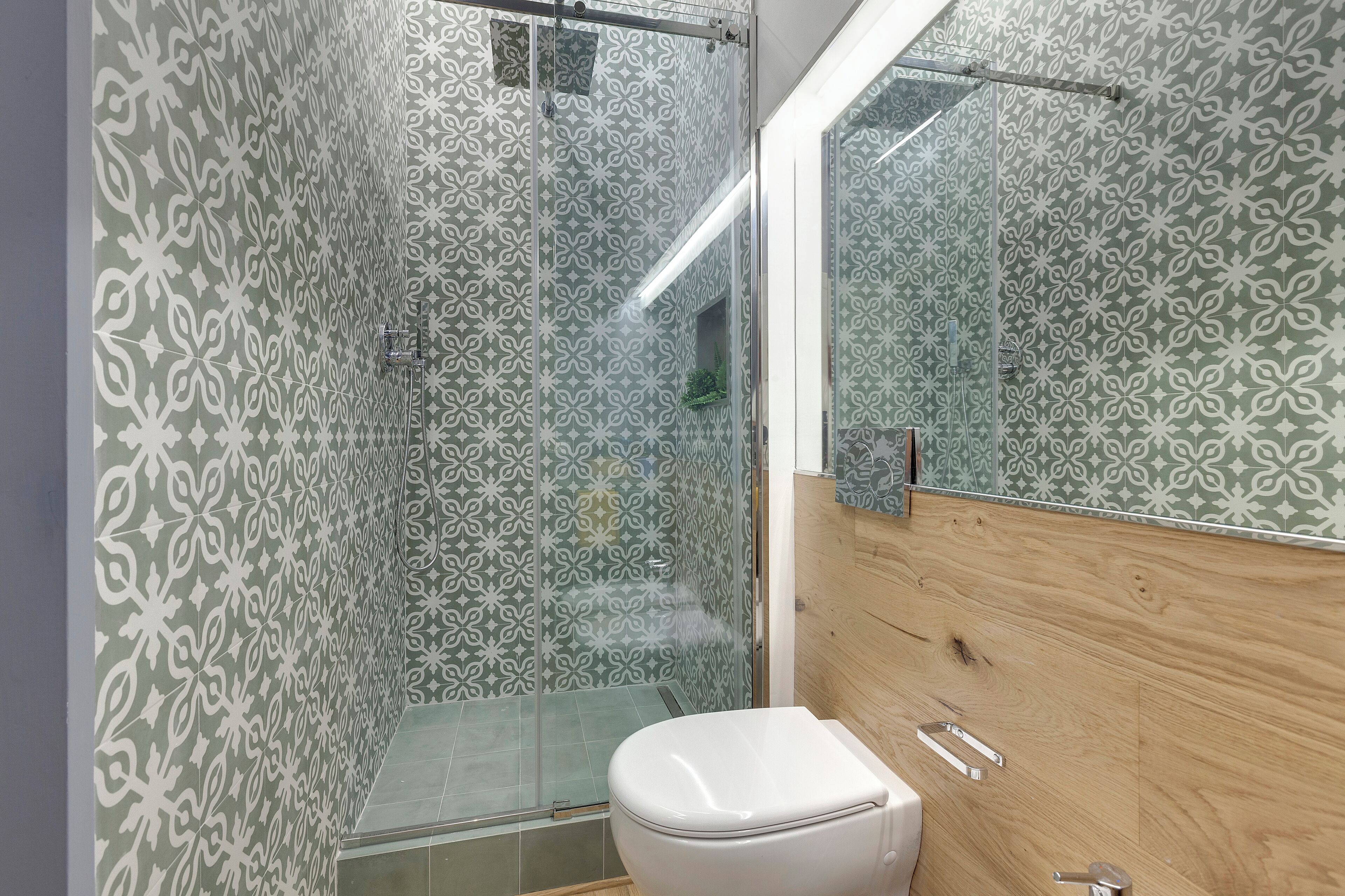 A bathroom with patterned walls, a glass shower enclosure, and a wooden vanity with a mirror.