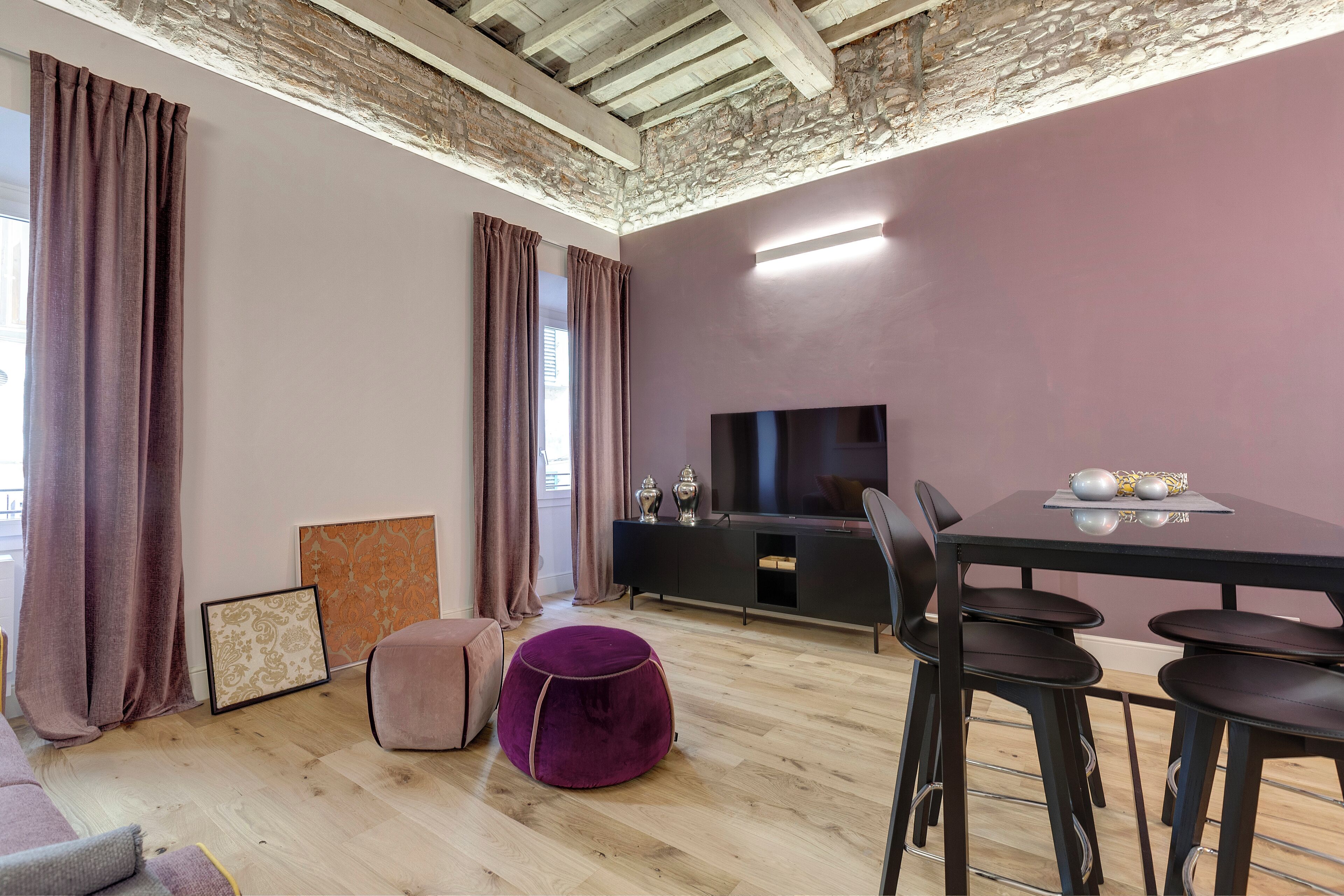 Un salon moderne avec un plafond en bois, un meuble TV noir, une table à manger avec quatre chaises et un pouf violet.