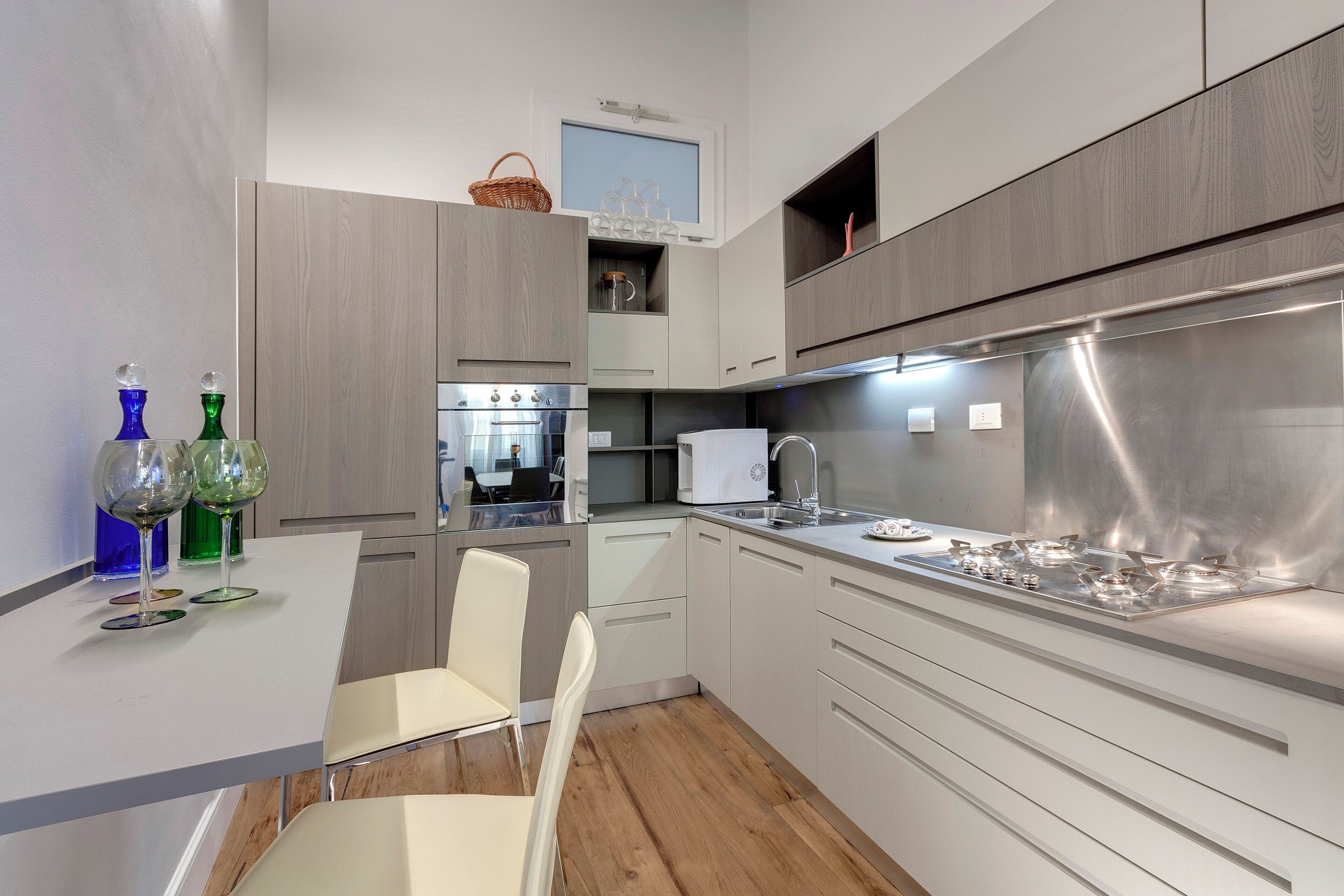 Una cocina moderna con armarios blancos, una estufa de acero inoxidable y un comedor con una silla blanca.