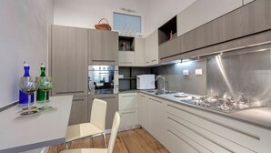 A modern kitchen with white cabinetry, a stainless steel stove, and a dining area with a white chair. - Mamo Florence - Anita Apartment (Florence)