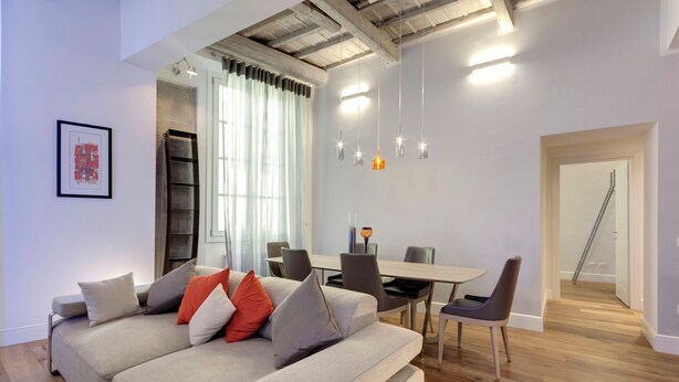 A modern living room with a sofa, dining table, and chairs. There is a staircase leading to another level. - Mamo Florence - Anita Apartment (Florence)