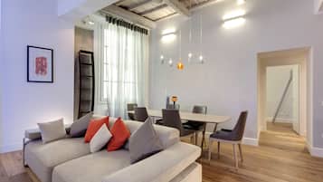 Una sala de estar moderna con un sofá, una mesa de comedor y sillas. Se ve una escalera que lleva a otro nivel.