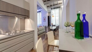 A modern kitchen with a stainless steel range hood, a dining area with a table and chairs, and two colorful glass bottles on the table. - Mamo Florence - Anita Apartment (Florence)