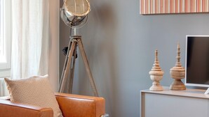 Een woonkamer met een leren bank, een vloerlamp, een televisie op een standaard en een decoratief wandobject.