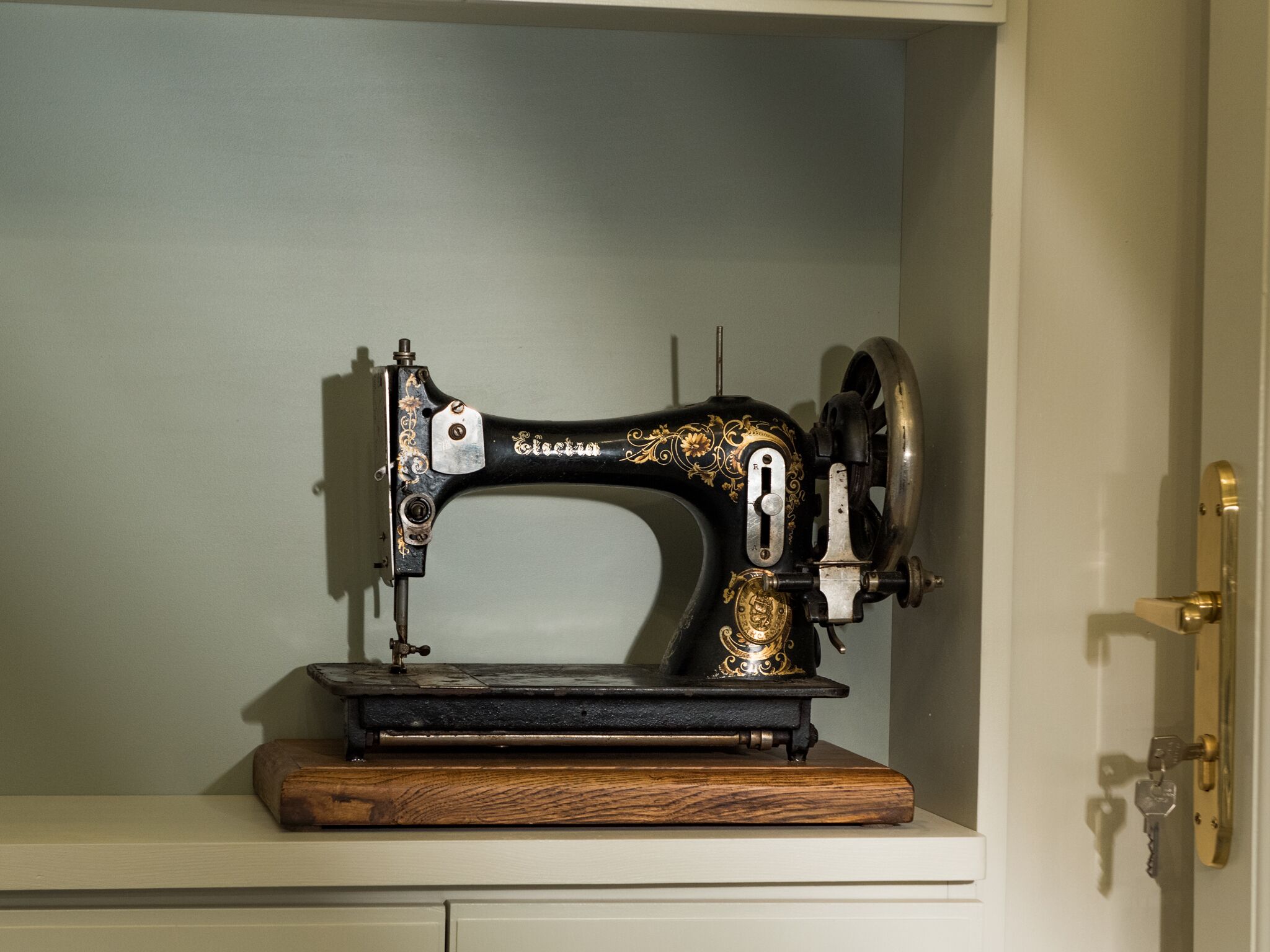 A vintage sewing machine on a wooden base in a room with a white door and light-colored walls.