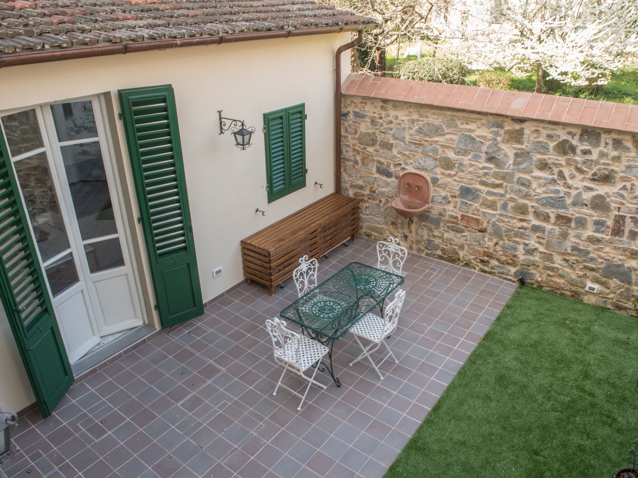 A patio with a stone wall, a wooden bench, and a table with chairs.