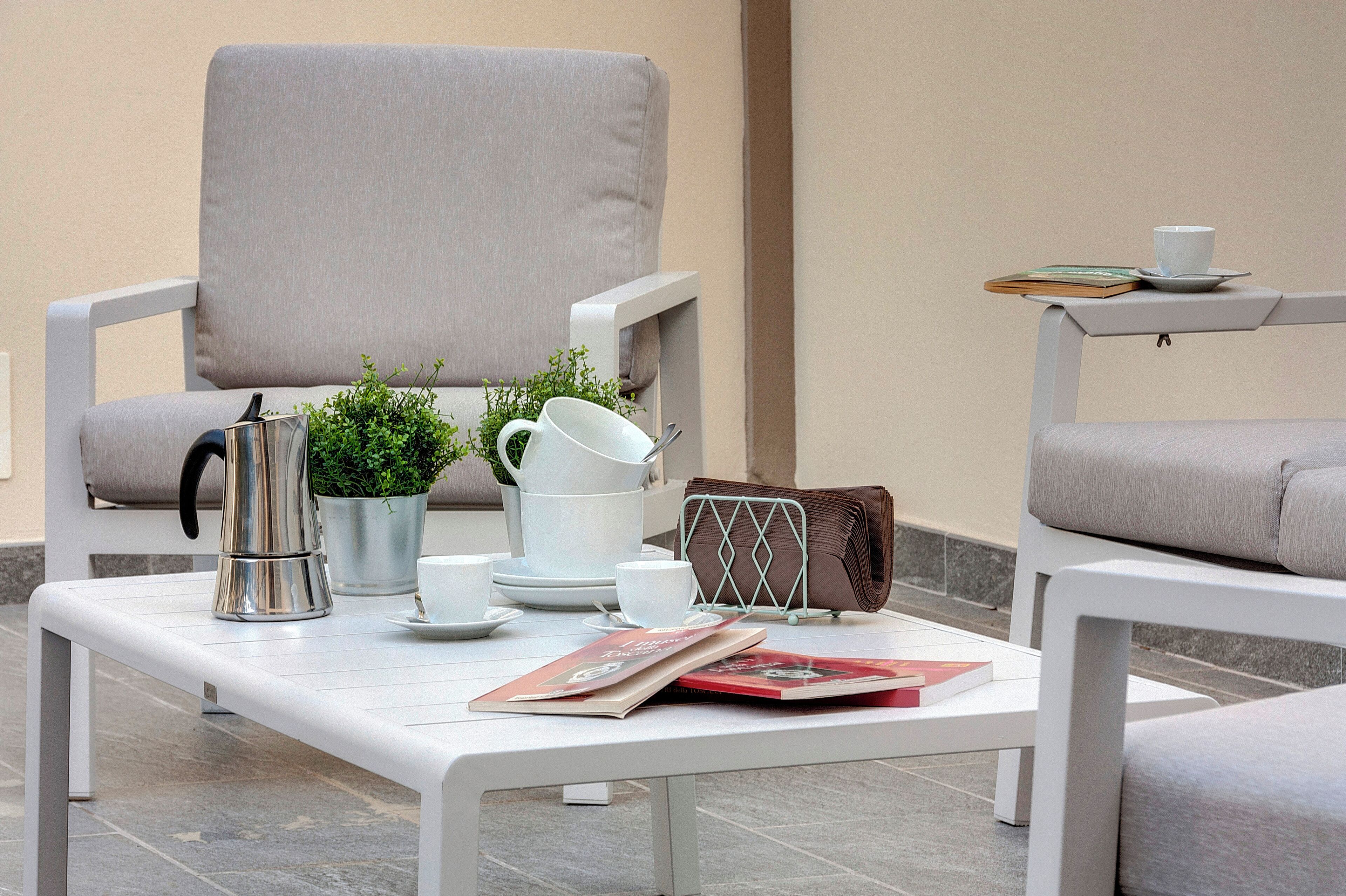 Een modern buitgedeelte met een witte tafel, een comfortabele stoel en een bijzettafeltje met een kopje en een boek.