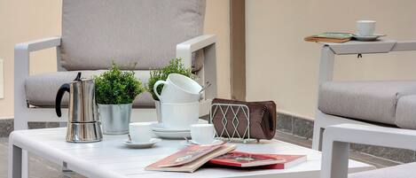 A modern outdoor seating area with a white table, a cushioned chair, and a small side table with a cup and book.