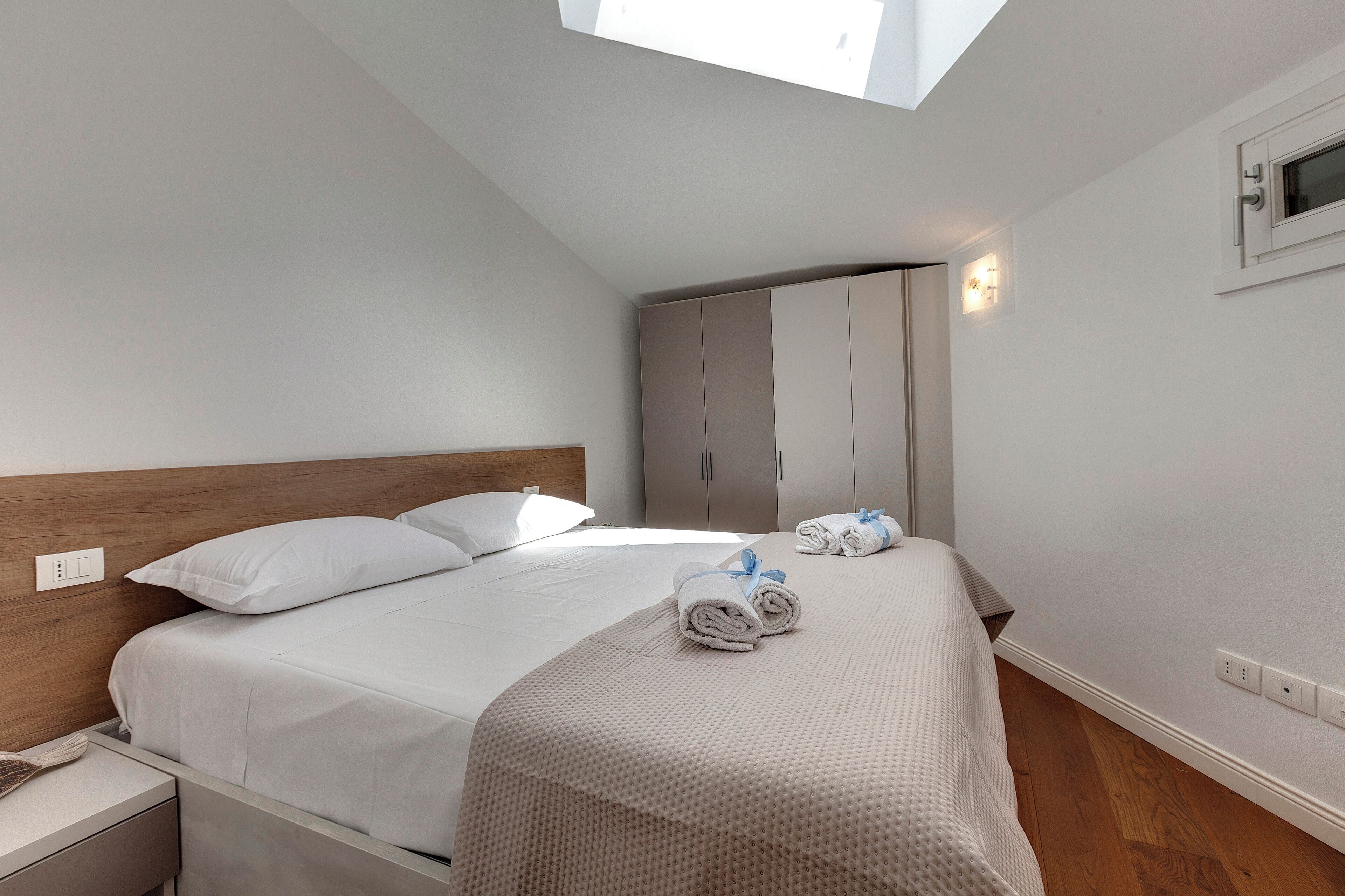 A bedroom with a skylight, a bed with white bedding, a nightstand, and a wardrobe.