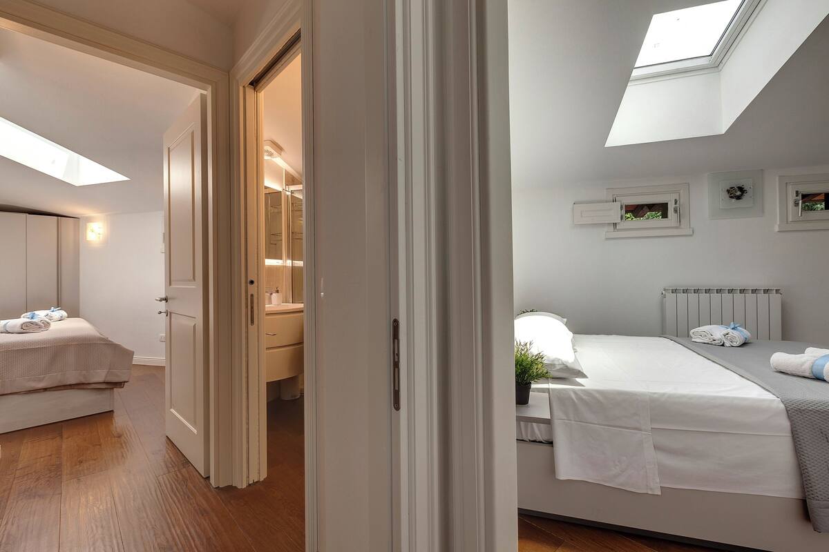 Un dormitorio con tragaluz, una cama, una mesita de noche y un ventanal pequeño.