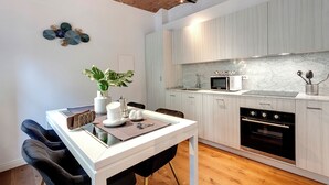 Una cocina moderna con armarios blancos, encimera de mármol, horno empotrado y un comedor con mesa blanca y sillas negras.