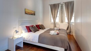Una cama bien hecha con almohadas, una lámpara de noche y una ventana con cortinas.