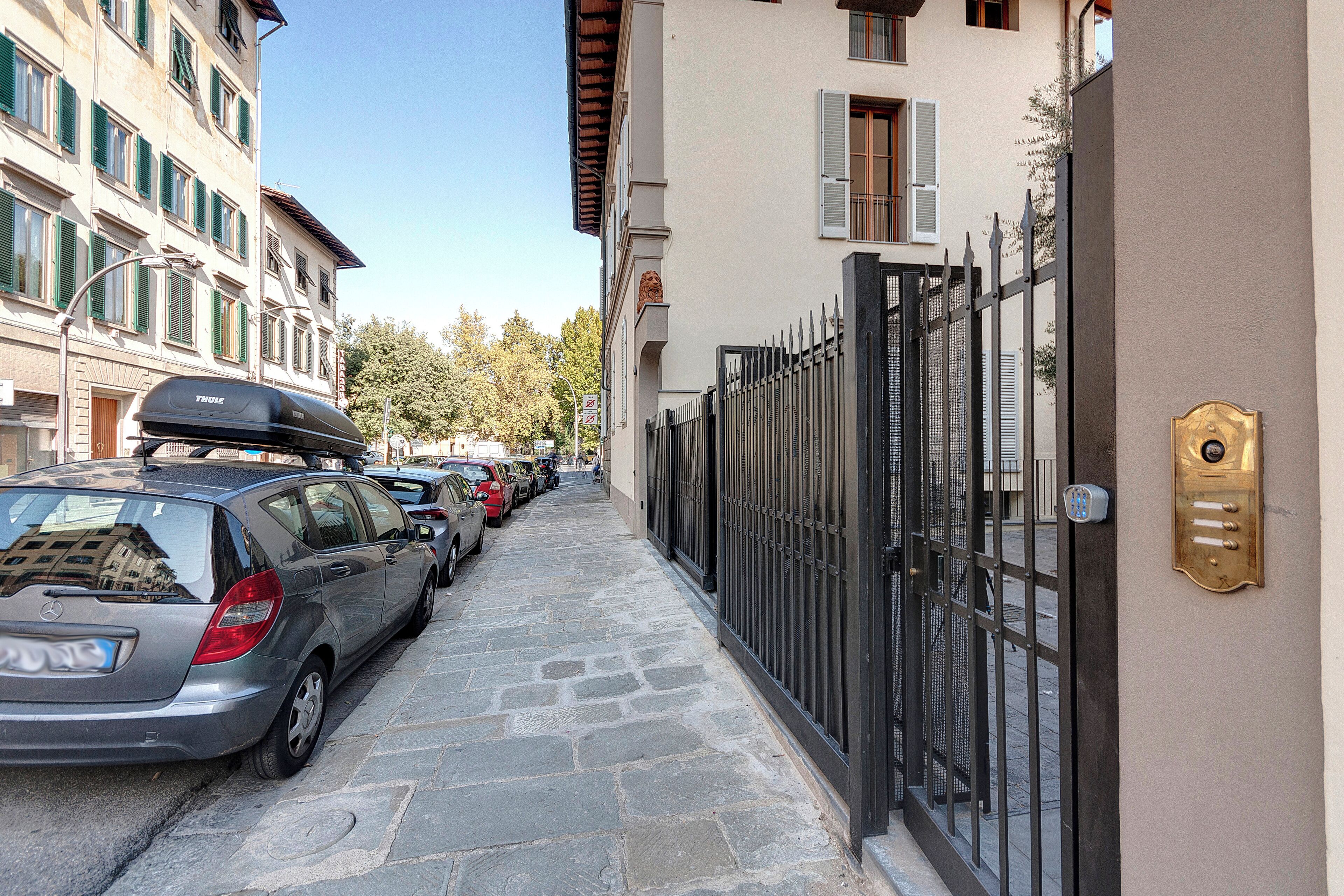 A narrow street lined with parked cars and a building with a gated entrance.