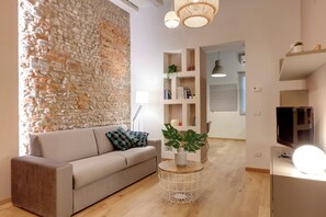 Un salon moderne avec un mur d’accent en pierre, un canapé beige, une table basse ronde agrémentée de plantes et un téléviseur posé sur un meuble.